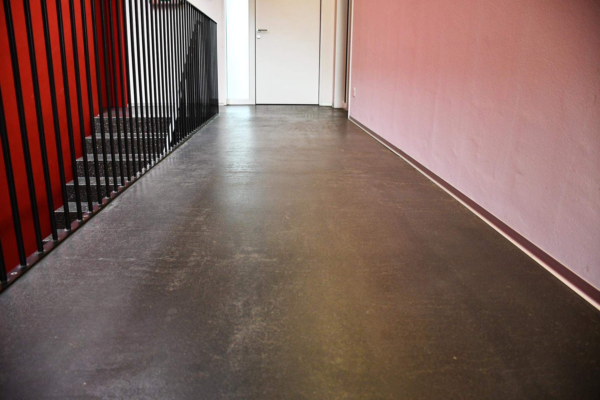 Betonboden: Ein eleganter, dunkler Zementüberzug zwischen roten Wänden